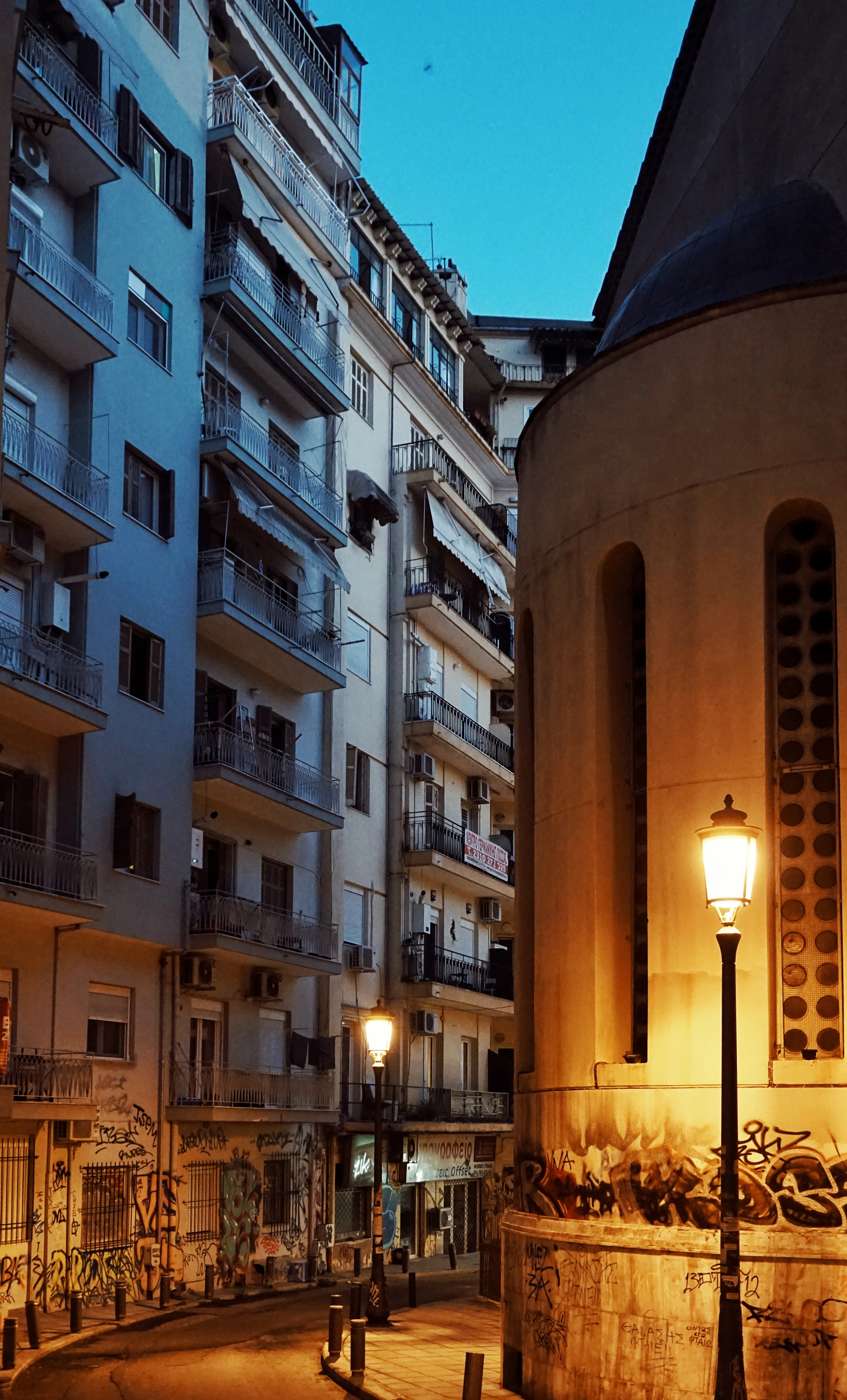 An old church and tall houses build directly next to it at night in Thessaloniki